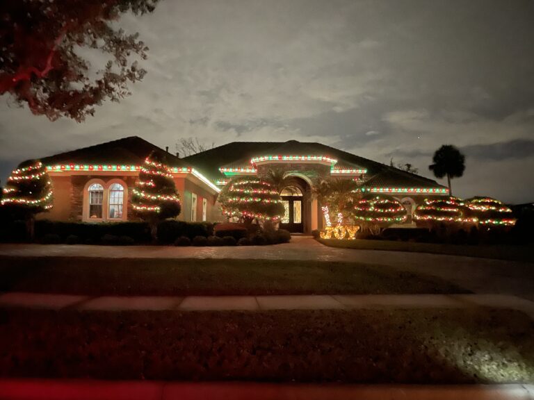 Garland and warm roofline lighting across the arched entry of a single story home