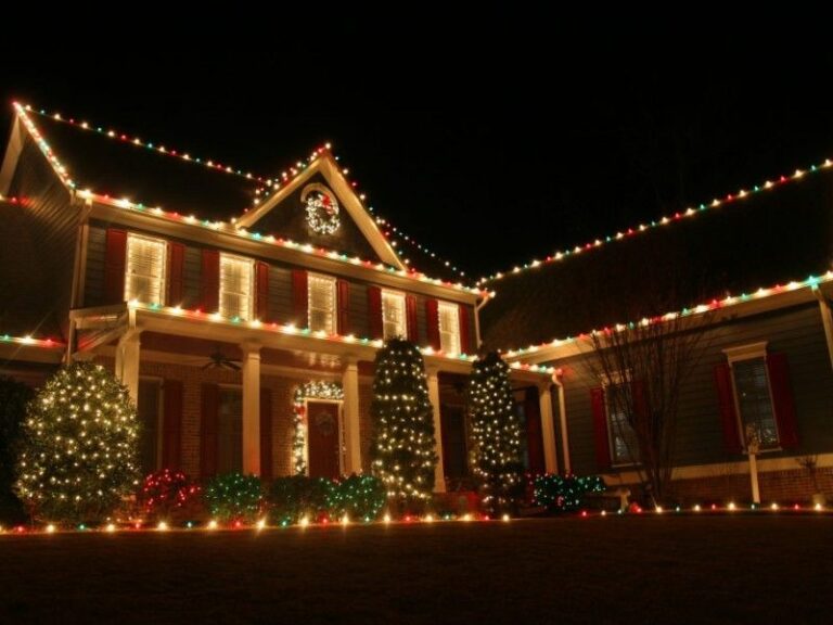 Single-story home with multicolor roofline lights and a lit wreath on the front gable